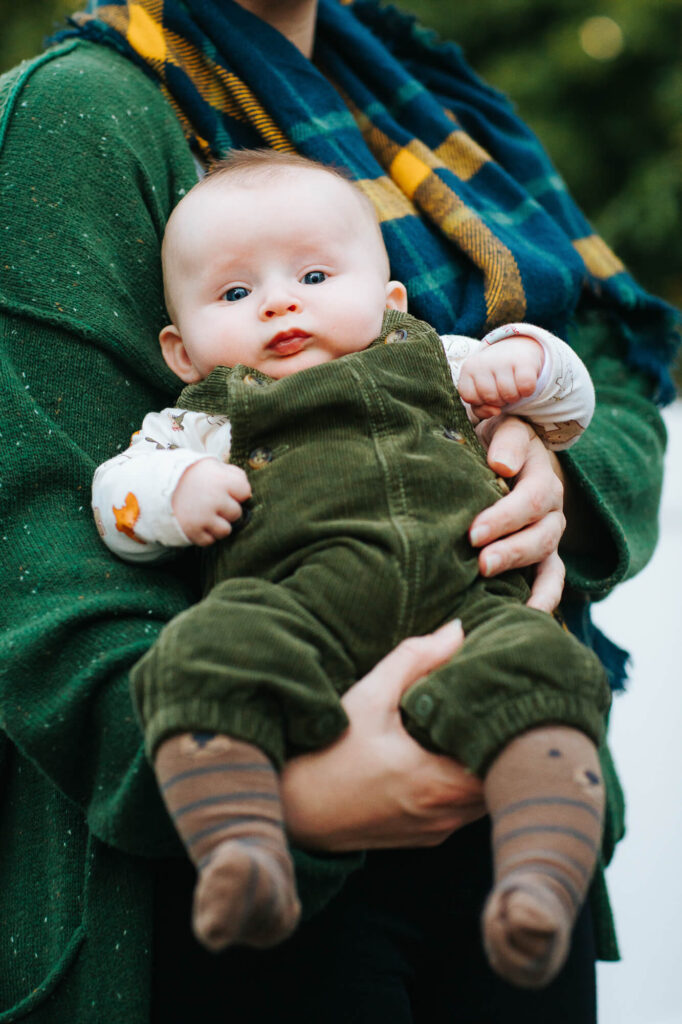 Red-haired baby in green corduroy overalls sits in a caretaker's arms