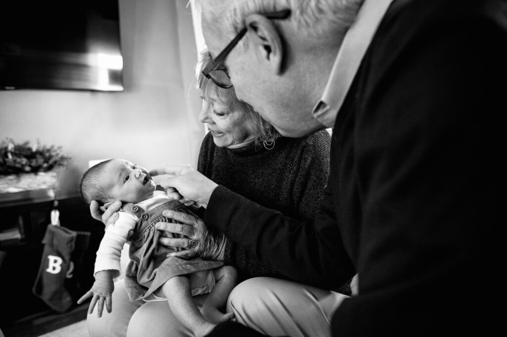 Black and white image of a grandmother and grandfather holding a newborn baby and smiling