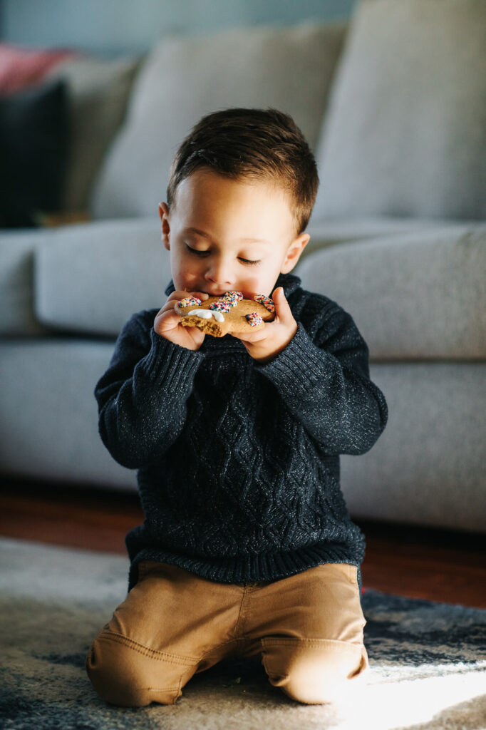 4 year old boy sits in the living room of his Somerville MA home eating a gingerbread cookie in front of a grey couch