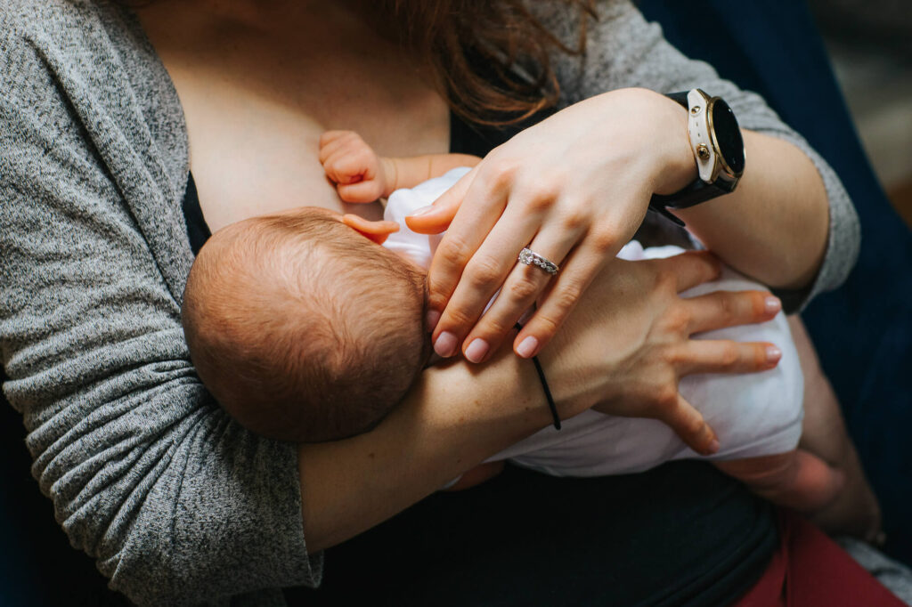 Newborn baby breastfeeds as mother strokes his head. We just see the back of his body and her arms holding him.