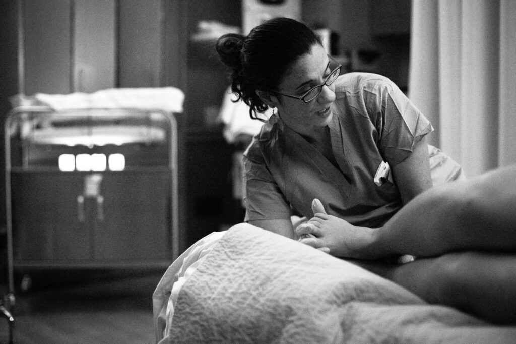 Black and white image of a midwife looking up at birthing woman's face right before her baby is delivered