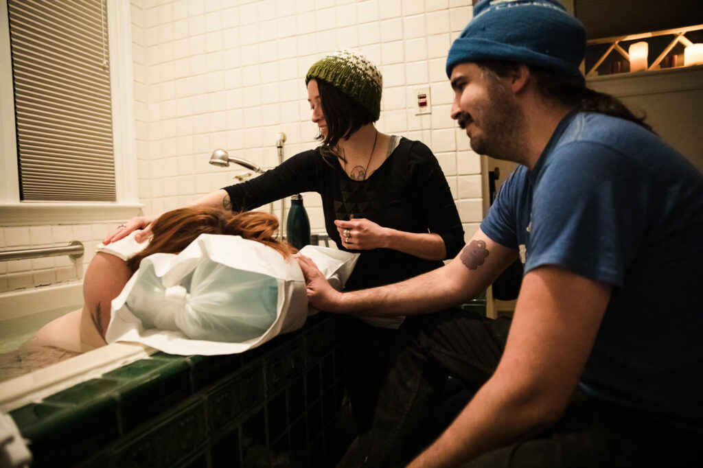 Doula comforts laboring woman as she leans forward in a birthing tub