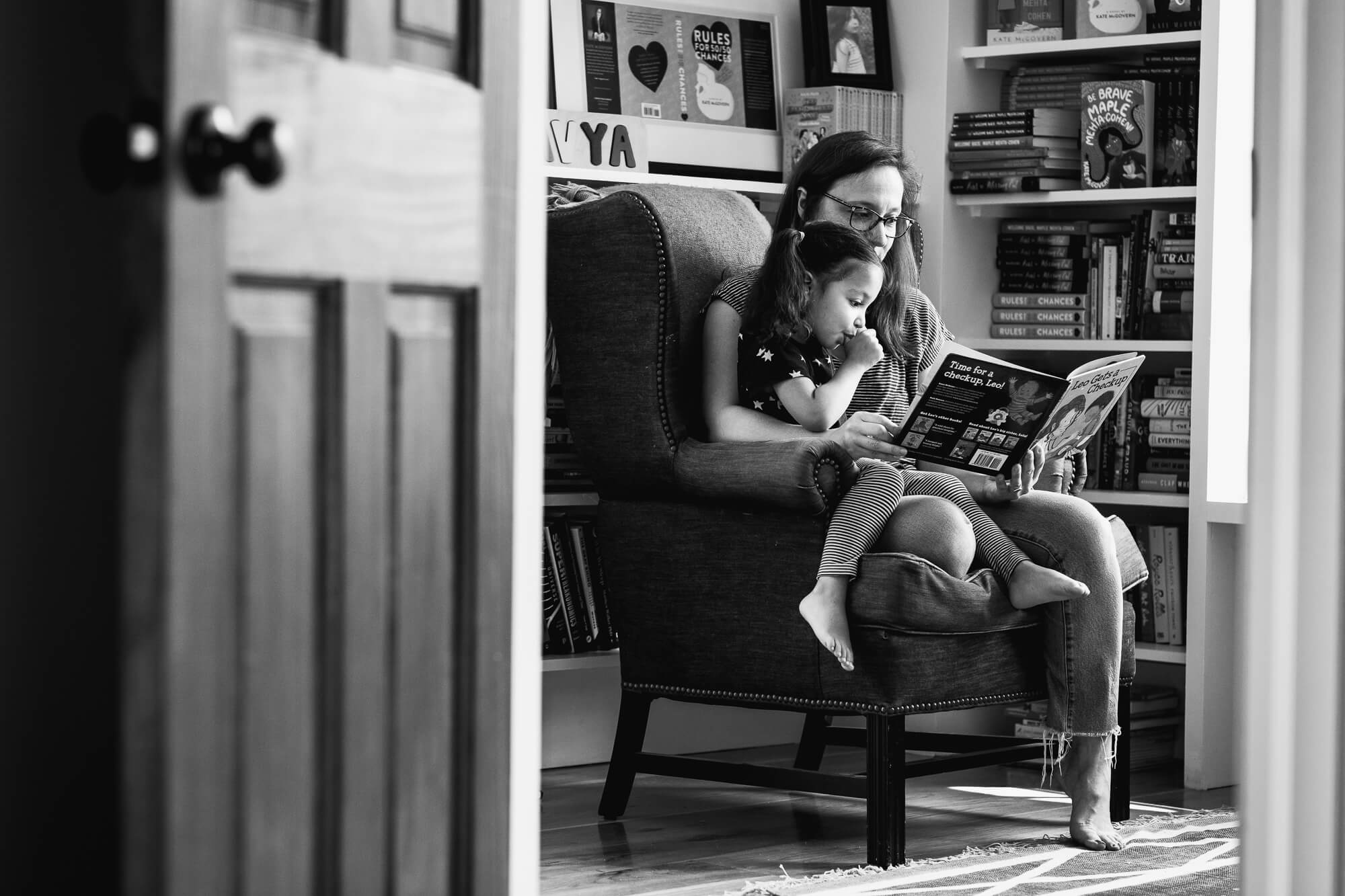 Black and white image of a mother reading to her daughter by a window in her office