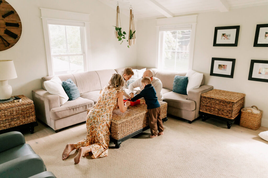 Blonde family is huddled around a coffee table in their living room, playing a board game.