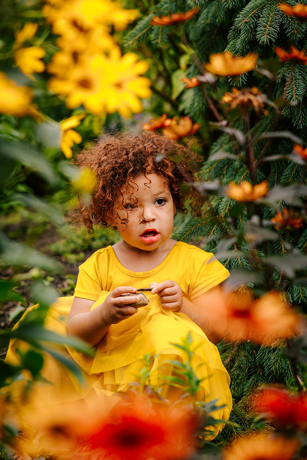 A toddler girl in a yellow dress explores a flower garden and rocks after visiting a Boston daycare