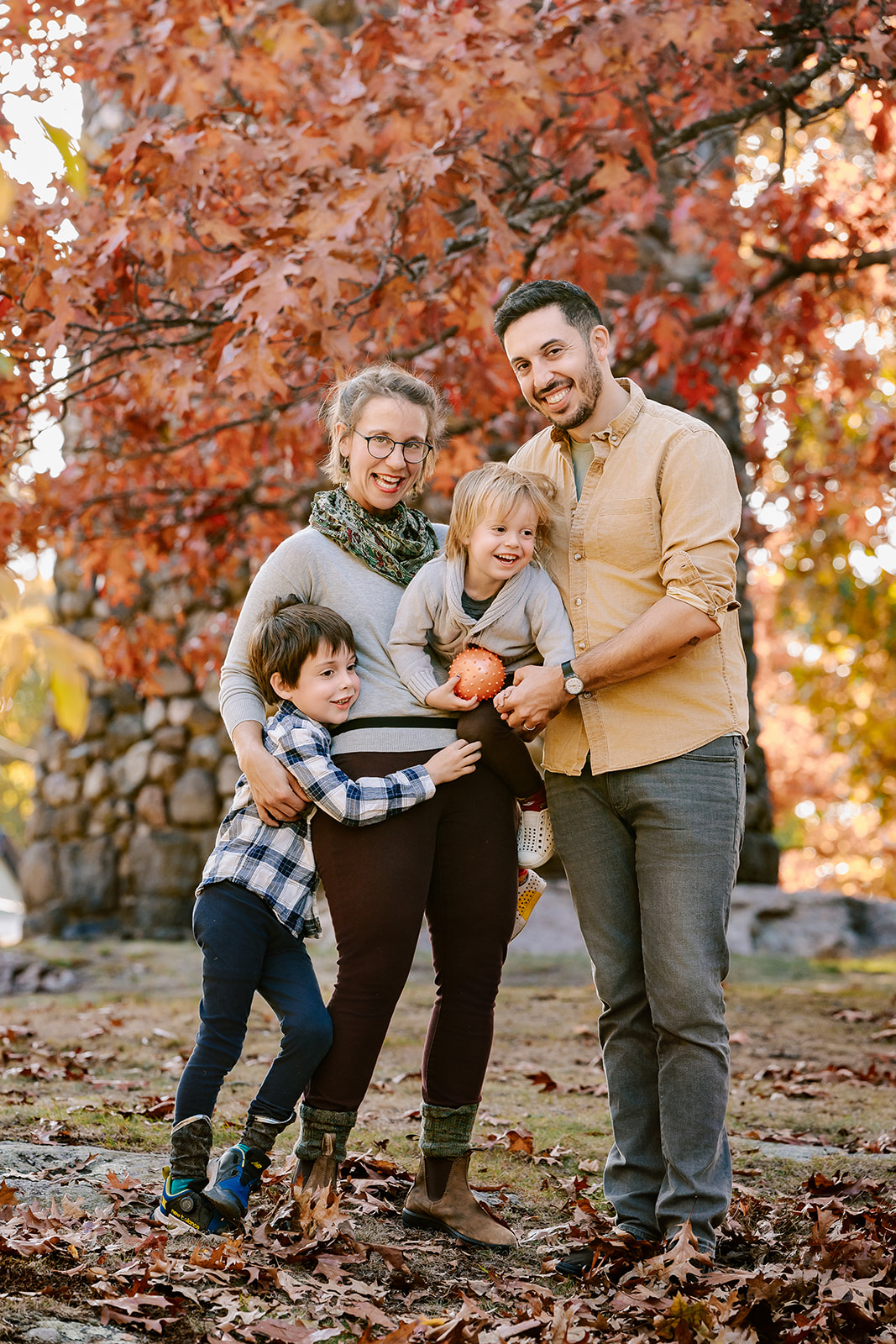 Two toddlers climb and play with mom and dad in a park at sunset in fall