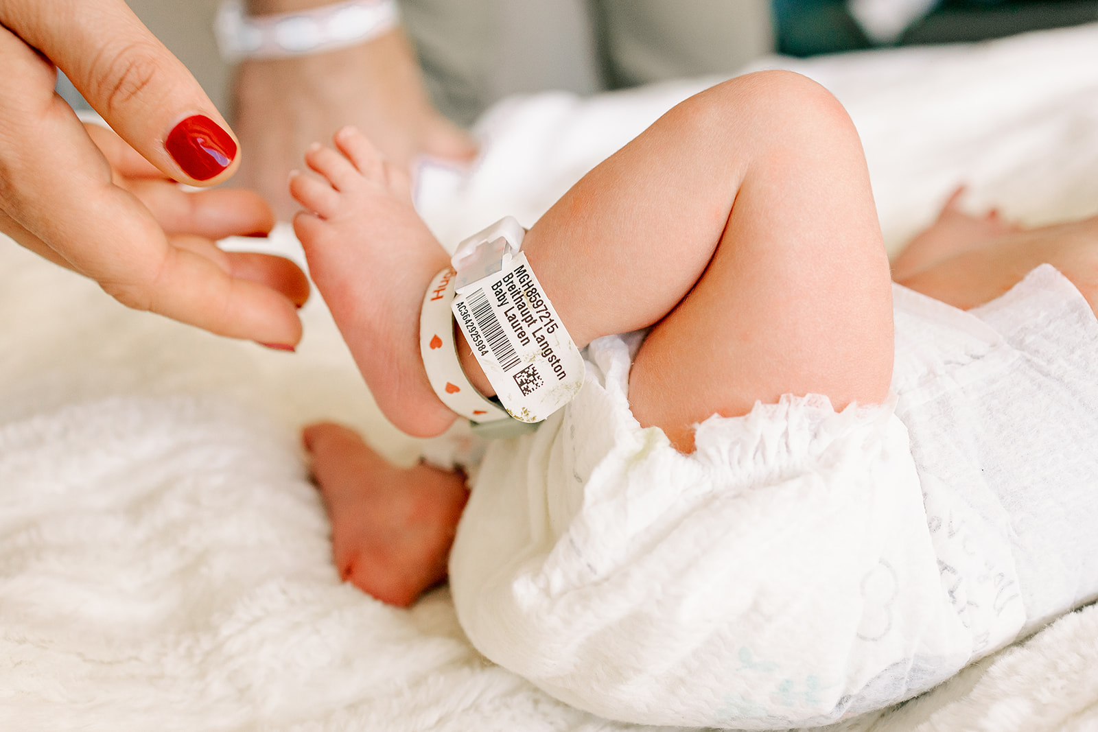 Details of mom reaching for a newborn's foot while laying in a bed in a diaper