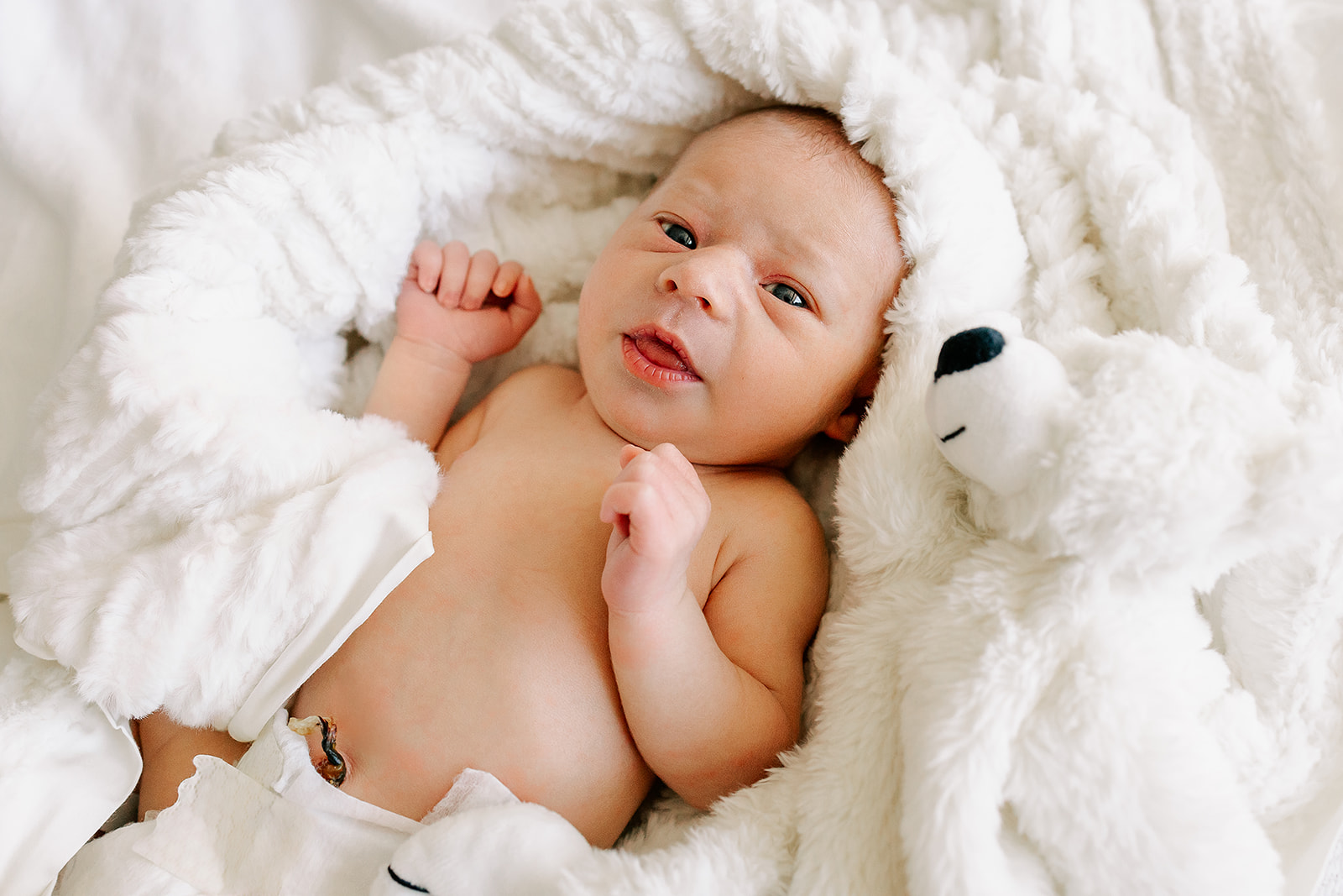 A newborn lays in a bed of white blankets with eyes and mouth open while using a diaper service in Boston