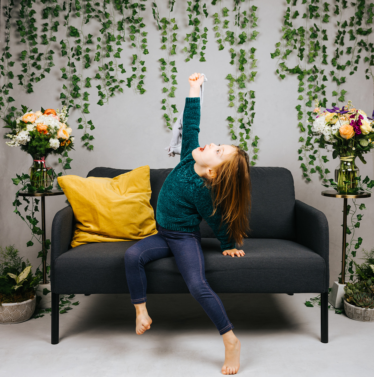 A happy young girl plays on a small couch in a studio with an arm raised before visiting indoor playgrounds in Boston