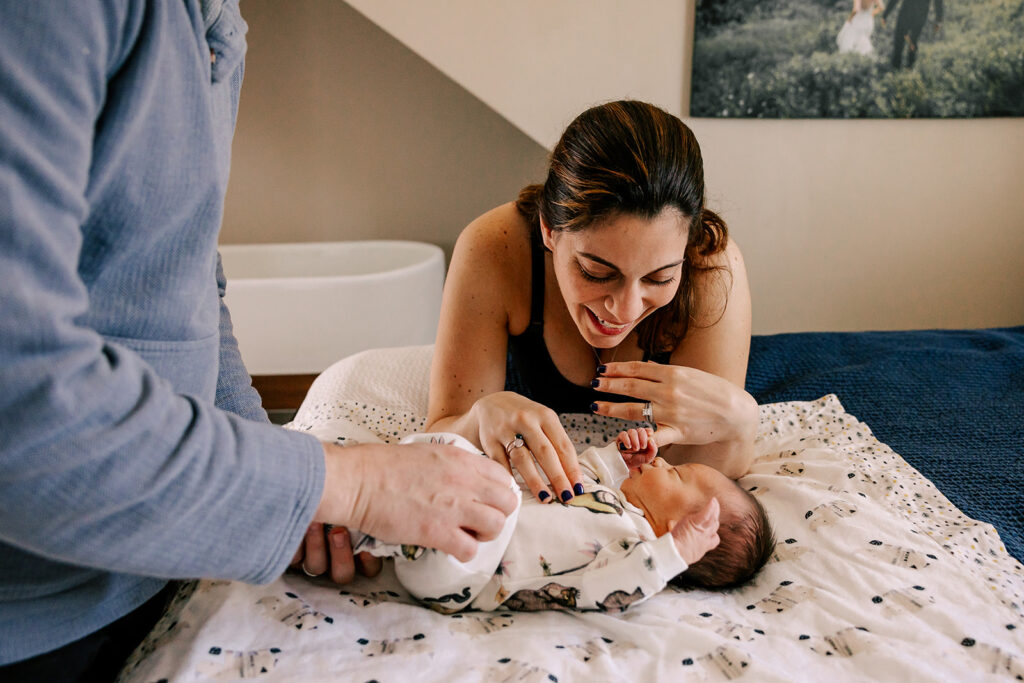 Happy new parents play with their newborn baby on a bed