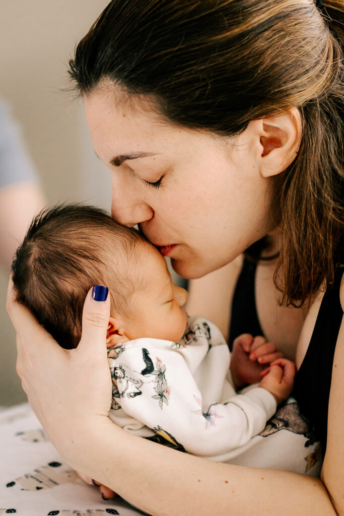 A newborn abby sleeps while mom leans in for a kiss after using a Midwife in Boston