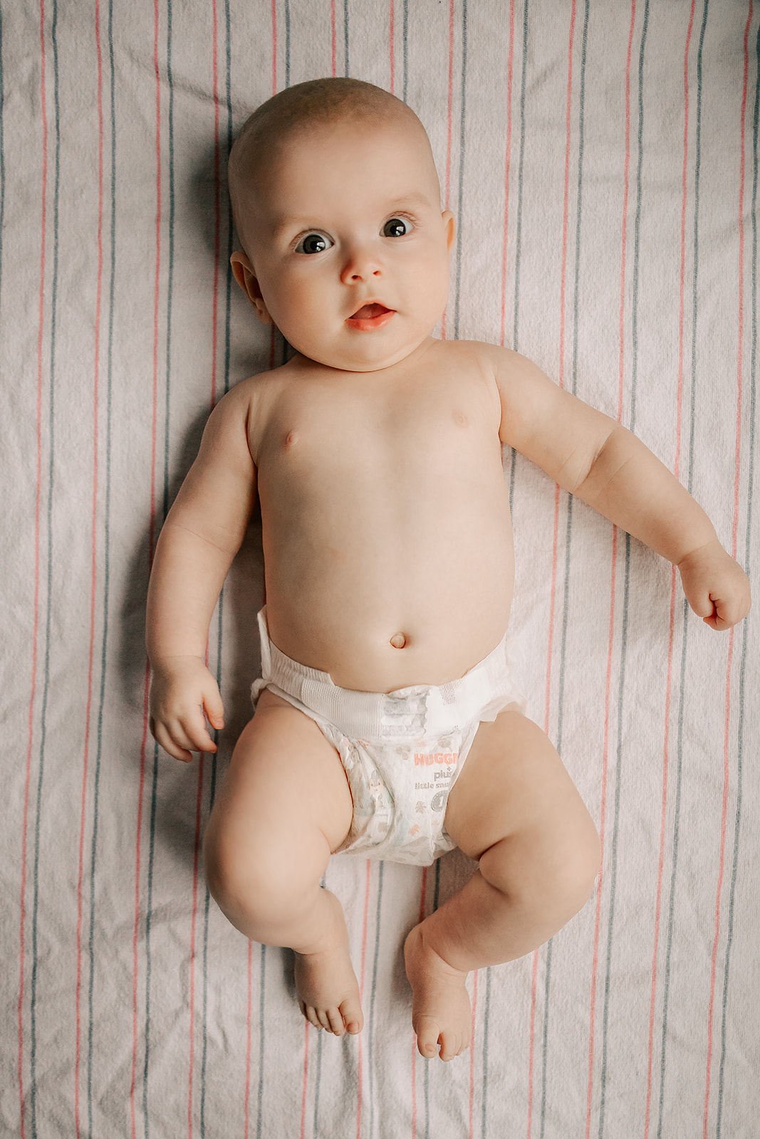 A happy baby in a diaper lays in a crib with eyes open