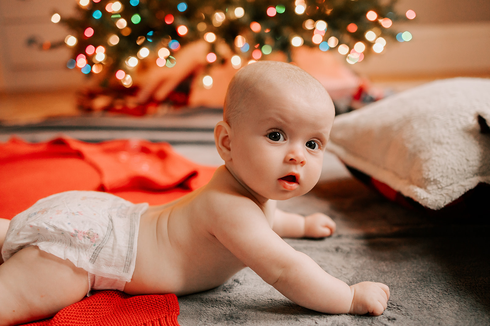 A newborn baby crawls under a christmas tree in a diaper thanks to an OBGYN in Boston