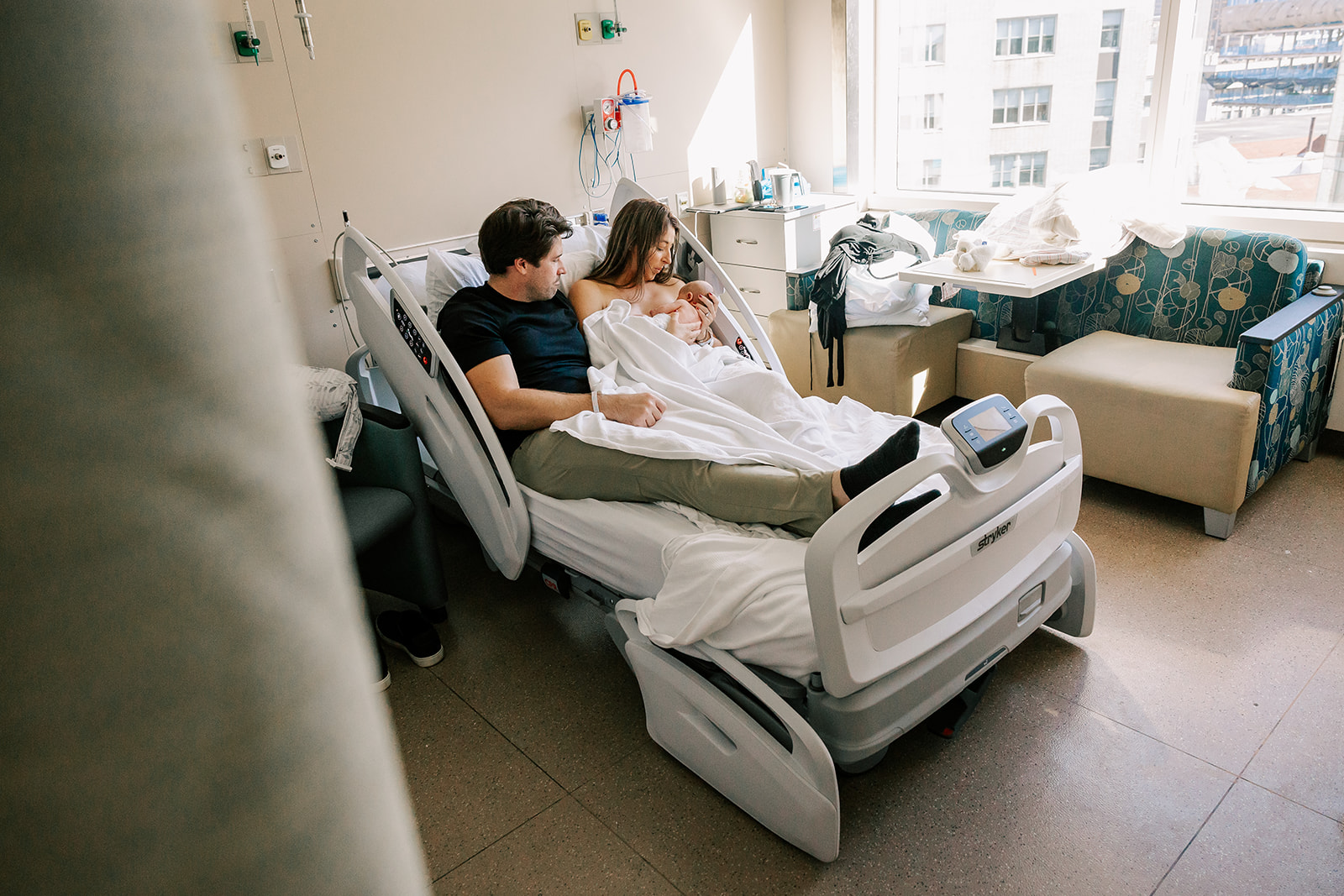 A mom nurses her newborn while laying in a hospital bed with dad after some parenting classes in Boston