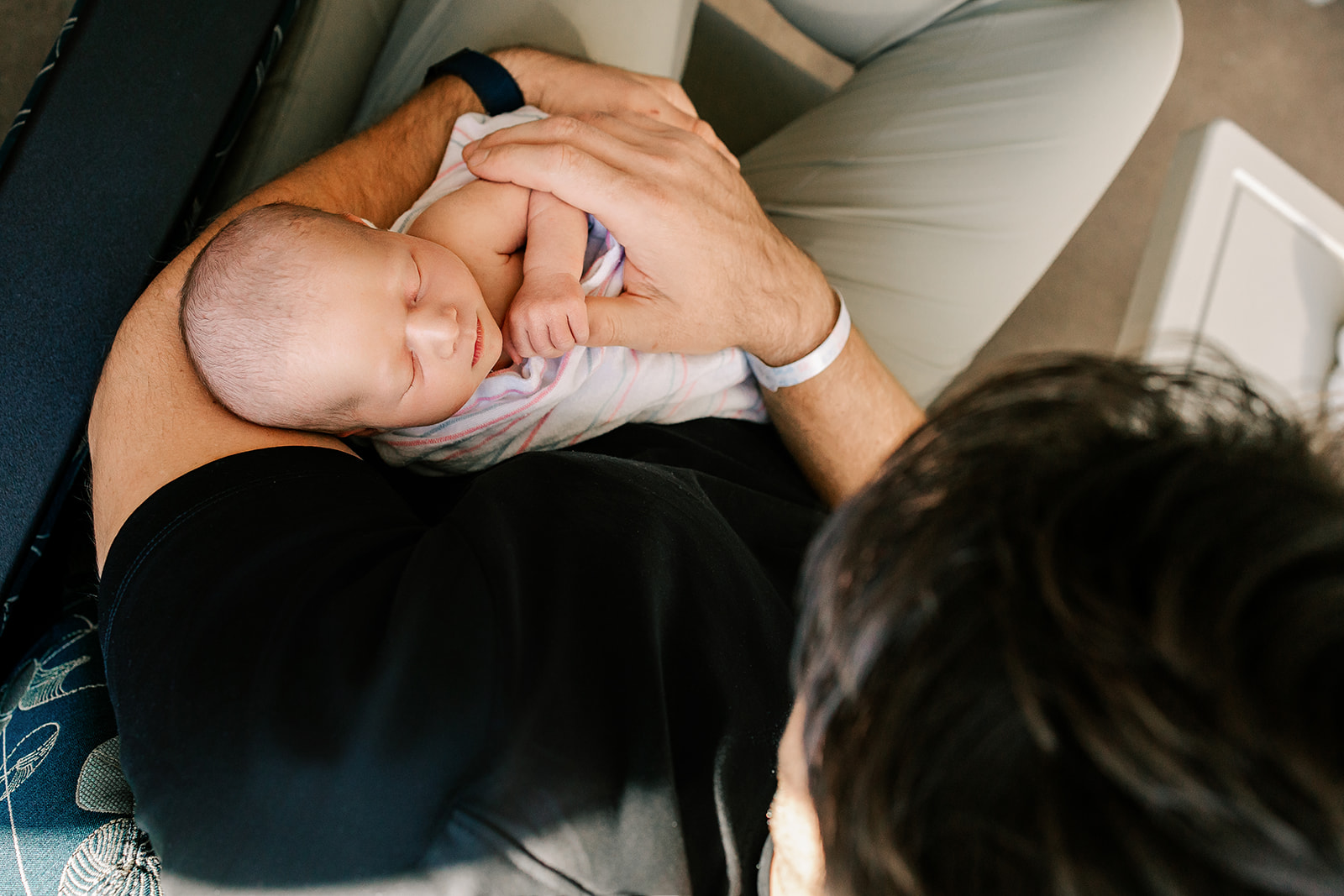 A newborn baby sleeps in dad's arms in a chair after some parenting classes in Boston