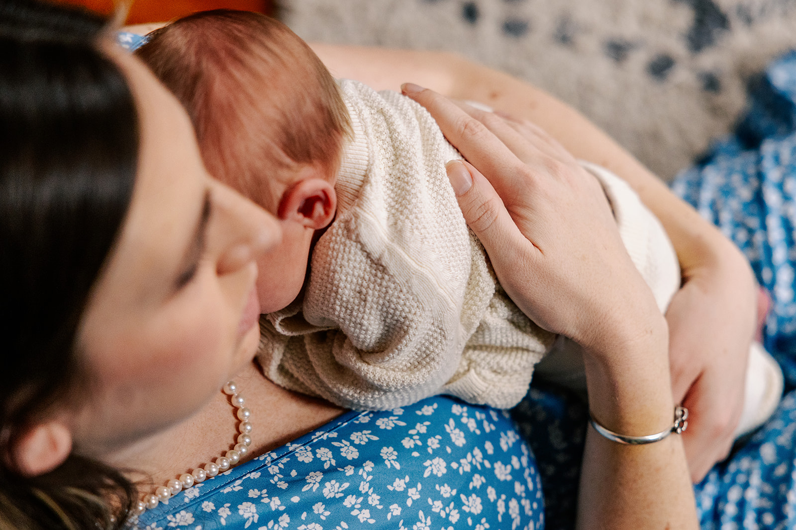 A mom in a blue dress cradles her newborn against her chest