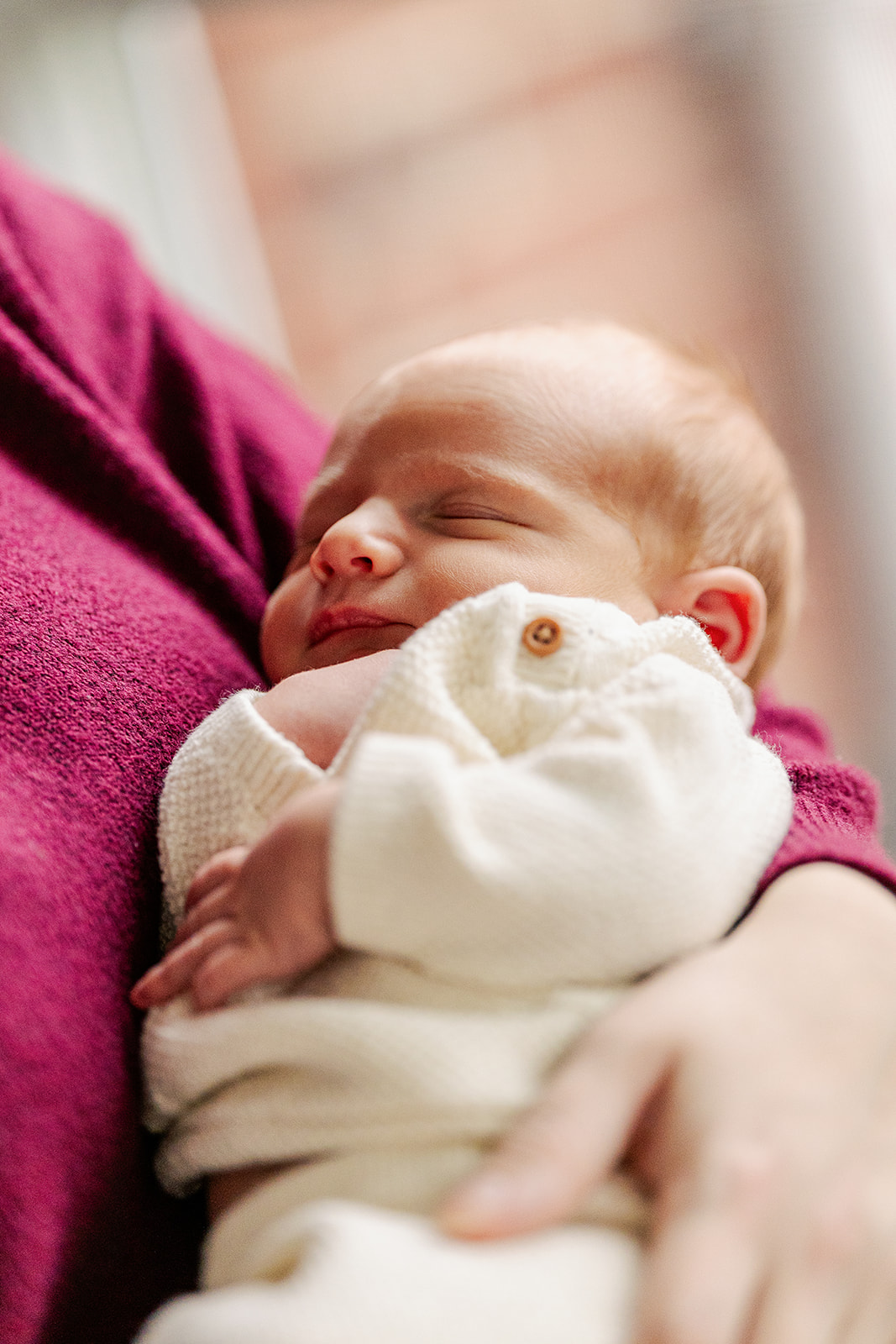 A newborn baby sleeps in a white onesie in mom's arms before she gets some pelvic floor therapy in Boston