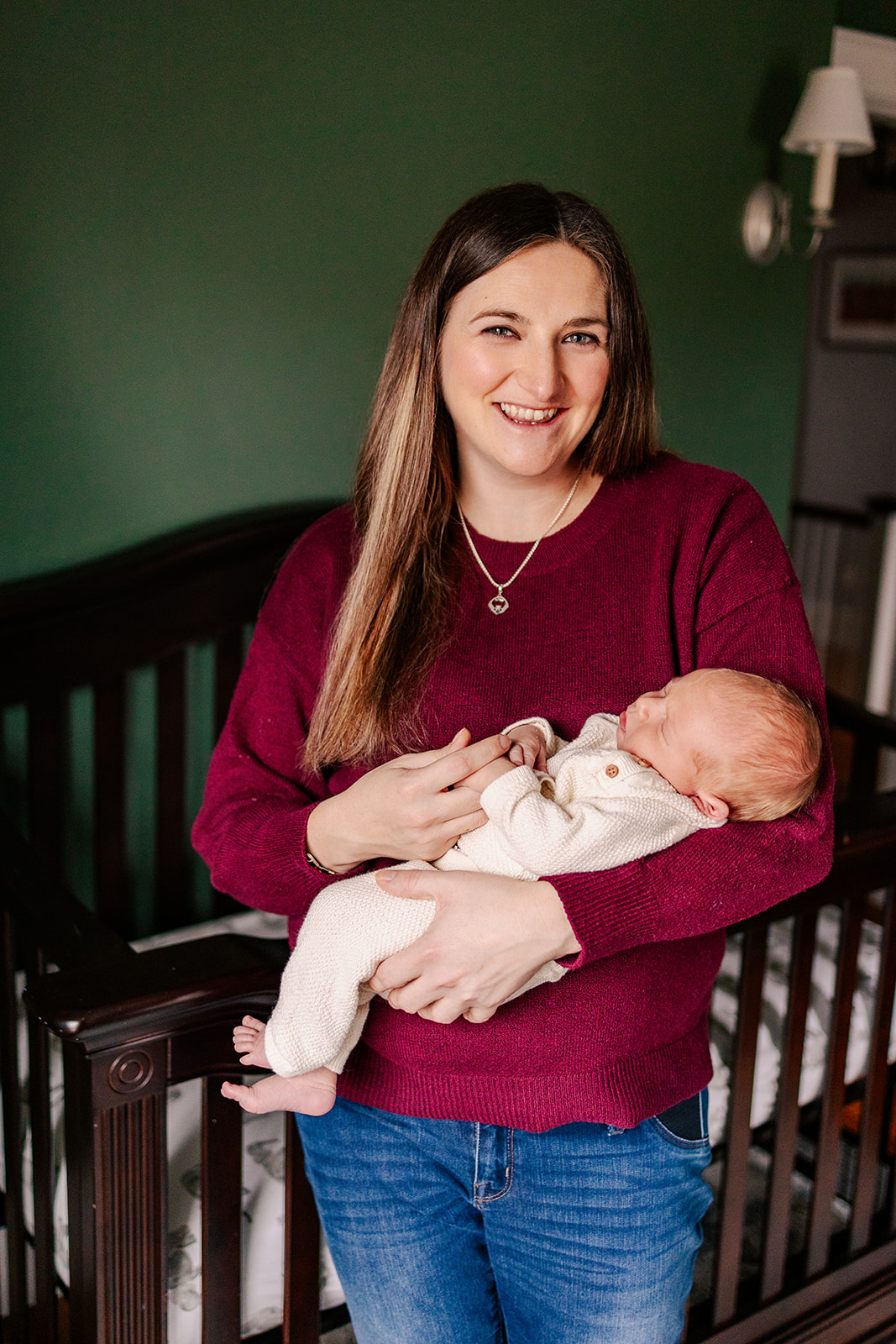 A happy new mom holds her sleeping newborn baby in her arms while standing in a nursery before some pelvic floor therapy in Boston