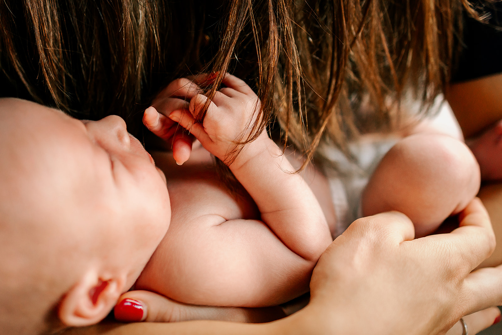 Details of a newborn baby holding mom's hair while laying in her arms after some placenta encapsulation in Boston