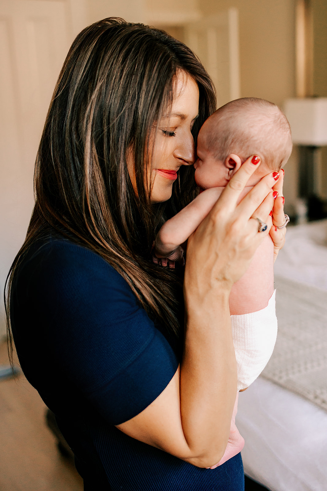 A happy new mom snuggles a newborn to her nose while standing in a bedroom after getting placenta encapsulation in Boston