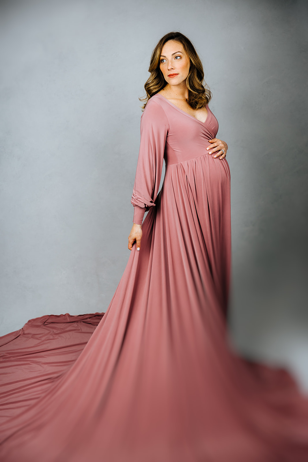 A mom to be turns in a long pink maternity gown in a studio