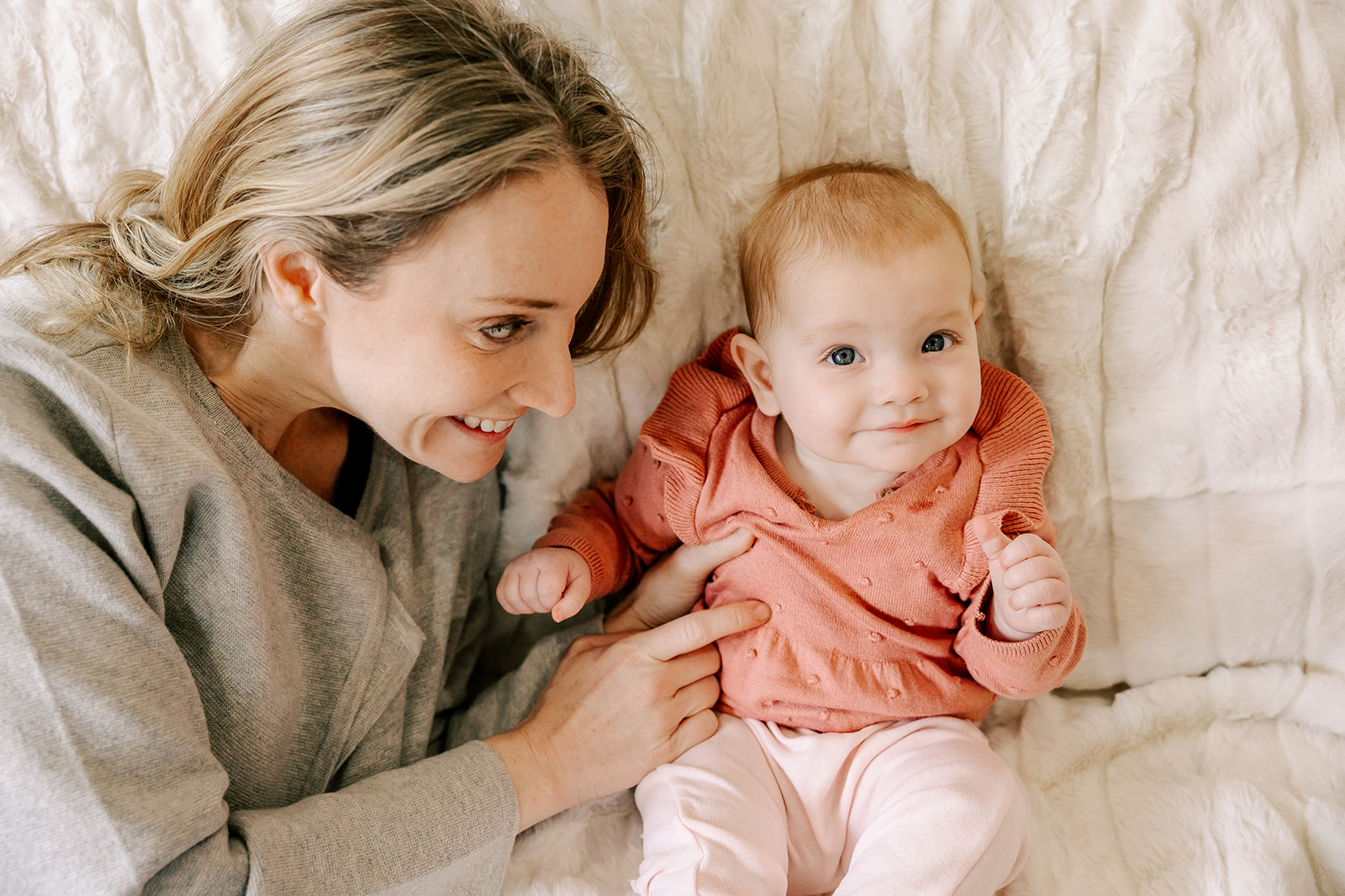 A happy mom tickles her baby on a bed