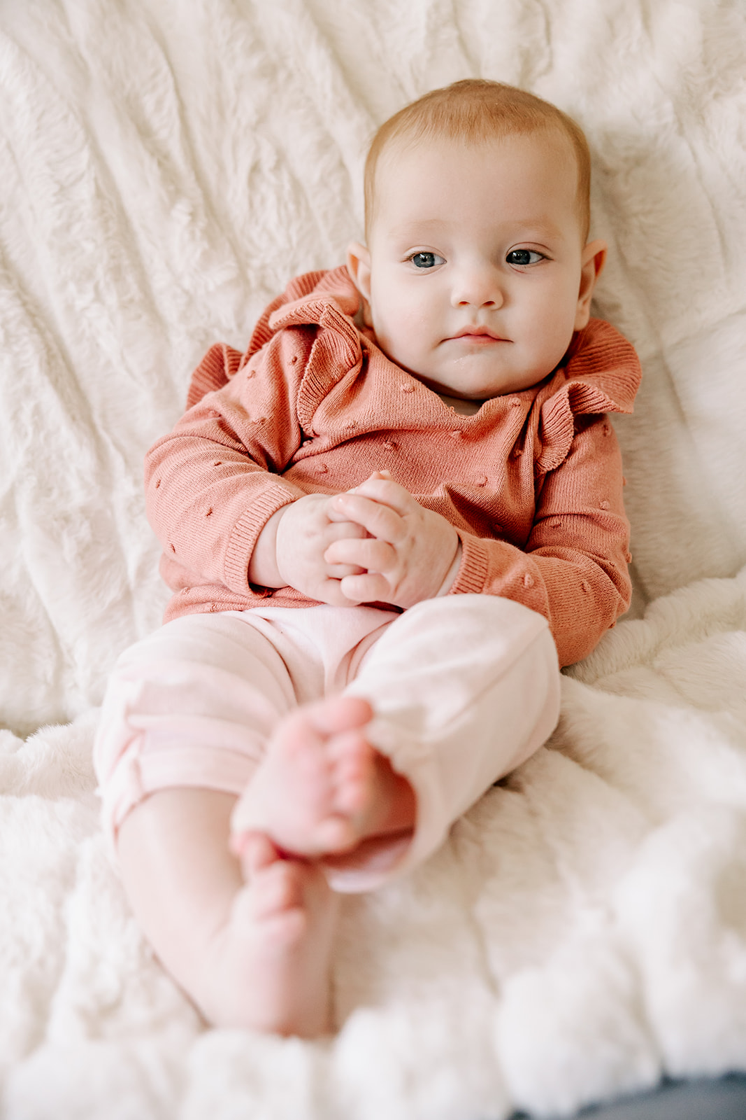 A baby in a pink sweater and pants lounges in a bed after some baby swim lessons in Boston