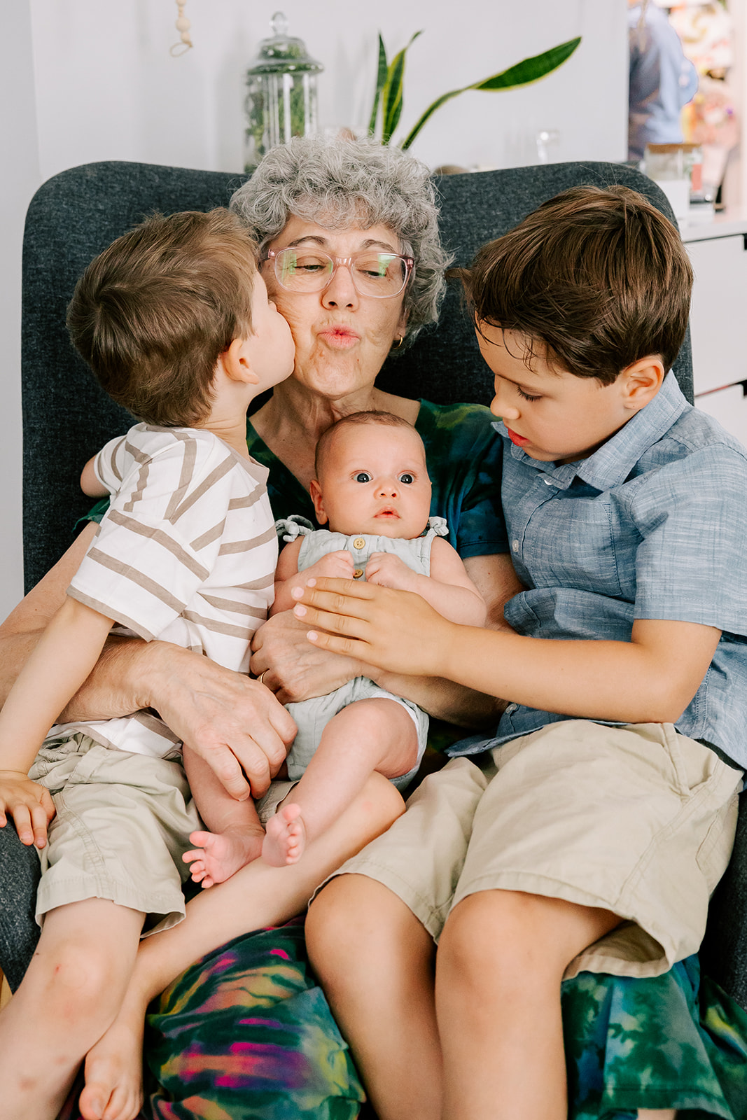 A happy grandma is kissed in a chair with her three grandsons in her lap after visiting Children's Museum in Boston