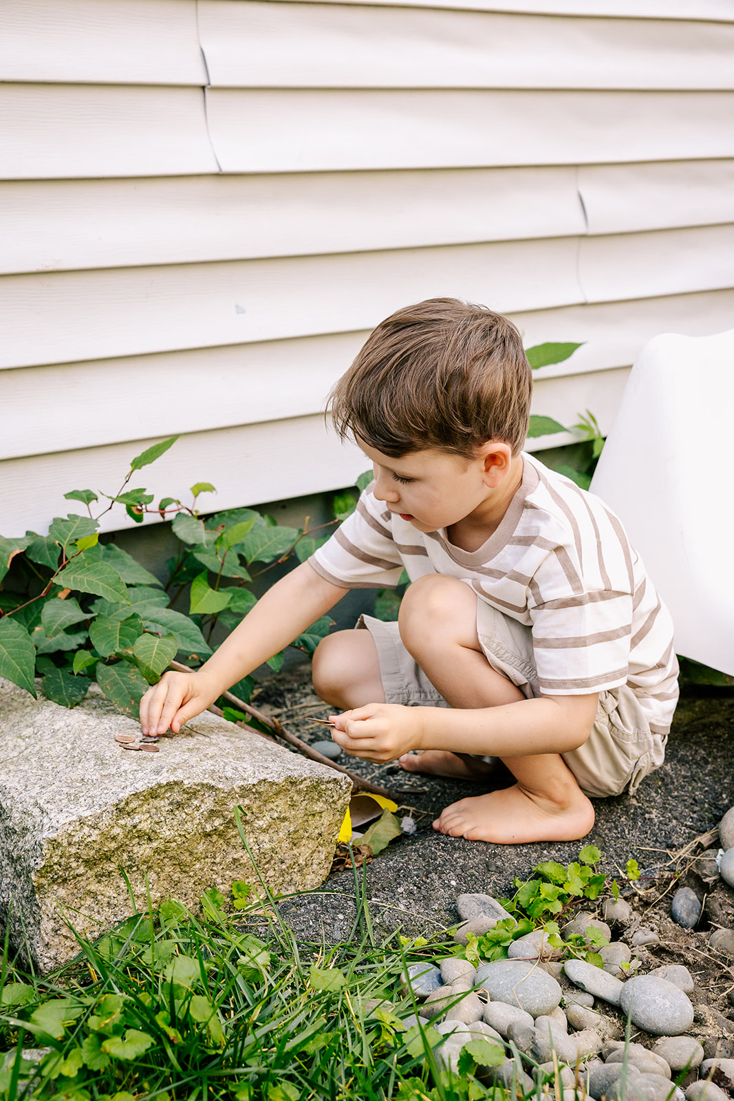 A young boy plays with coins in the garden on the side of his house after visiting Children's Museum in Boston