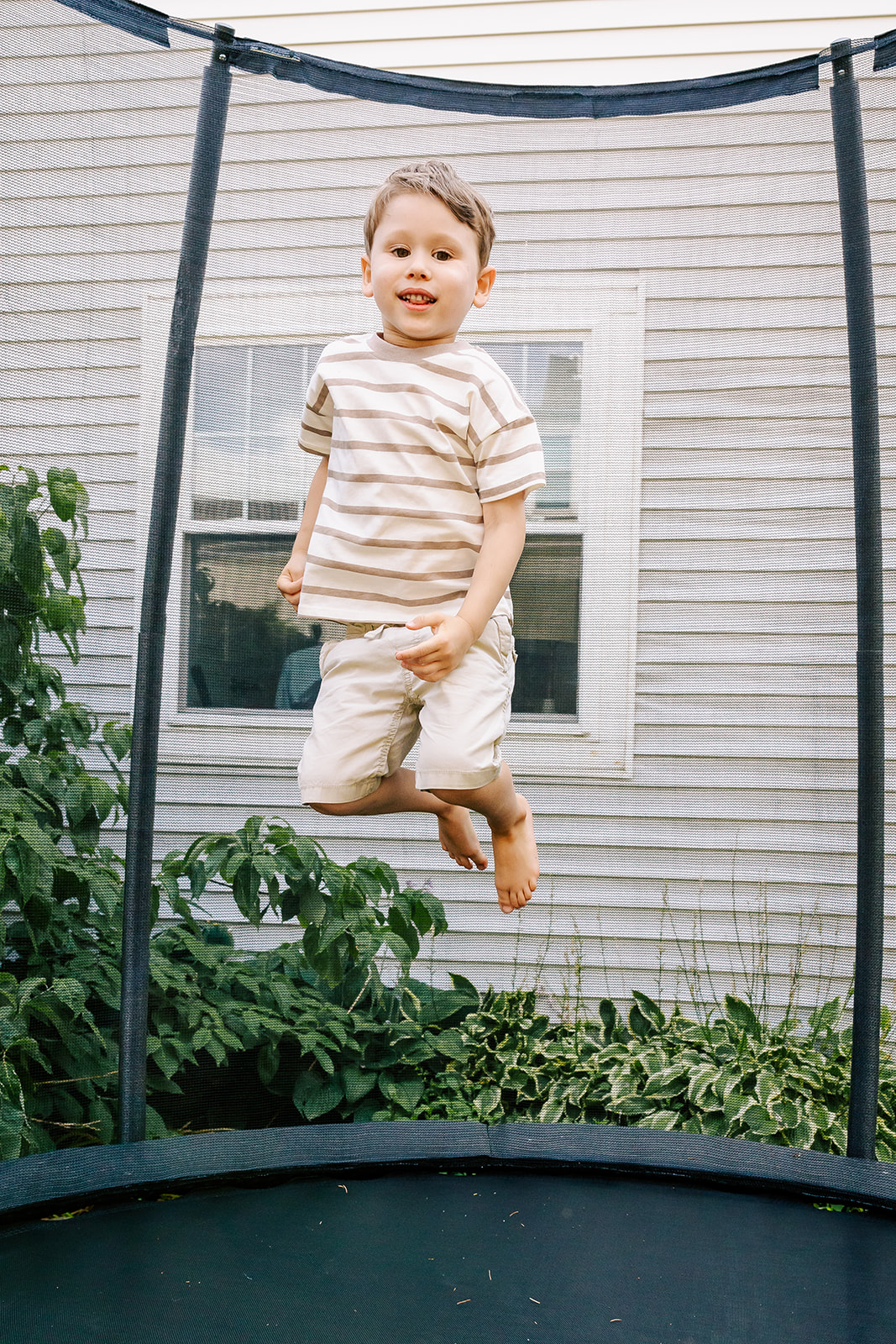 A happy toddler jumps on a trampoline in a stripe shirt before visiting Children's Museum in Boston