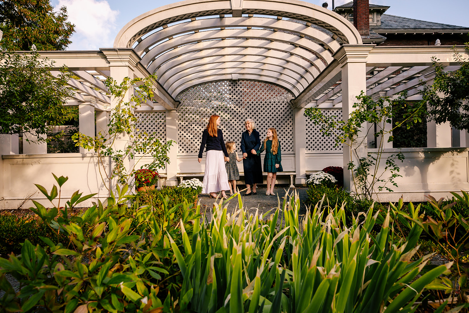 A grandma walks in a garden patio holding hands with her daughter and grand daughters while staying at kid-friendly hotels in Boston