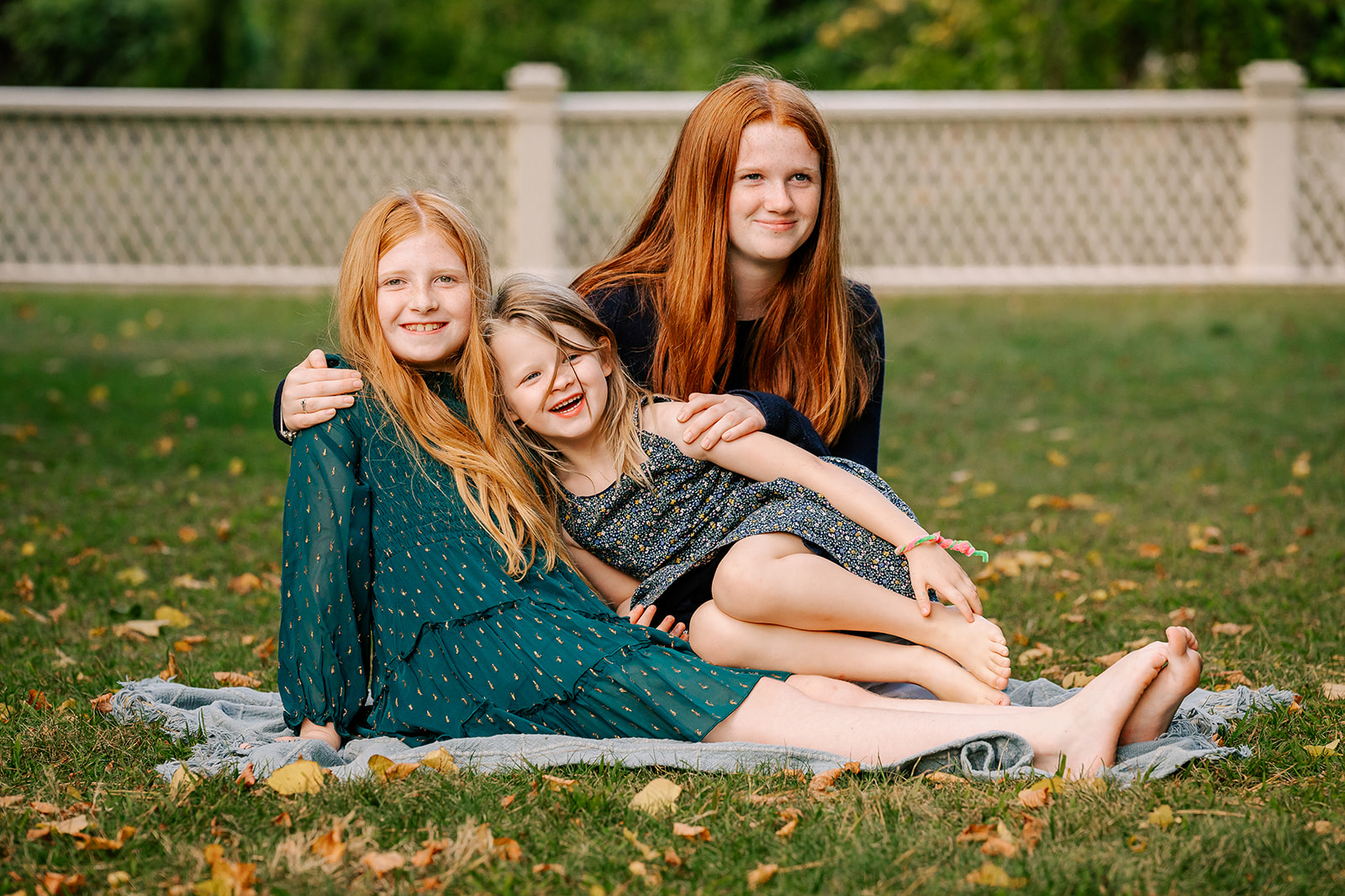 Three sisters cuddle and laugh on a picnic blanket in a park lawn at sunset while staying at kid-friendly hotels in Boston