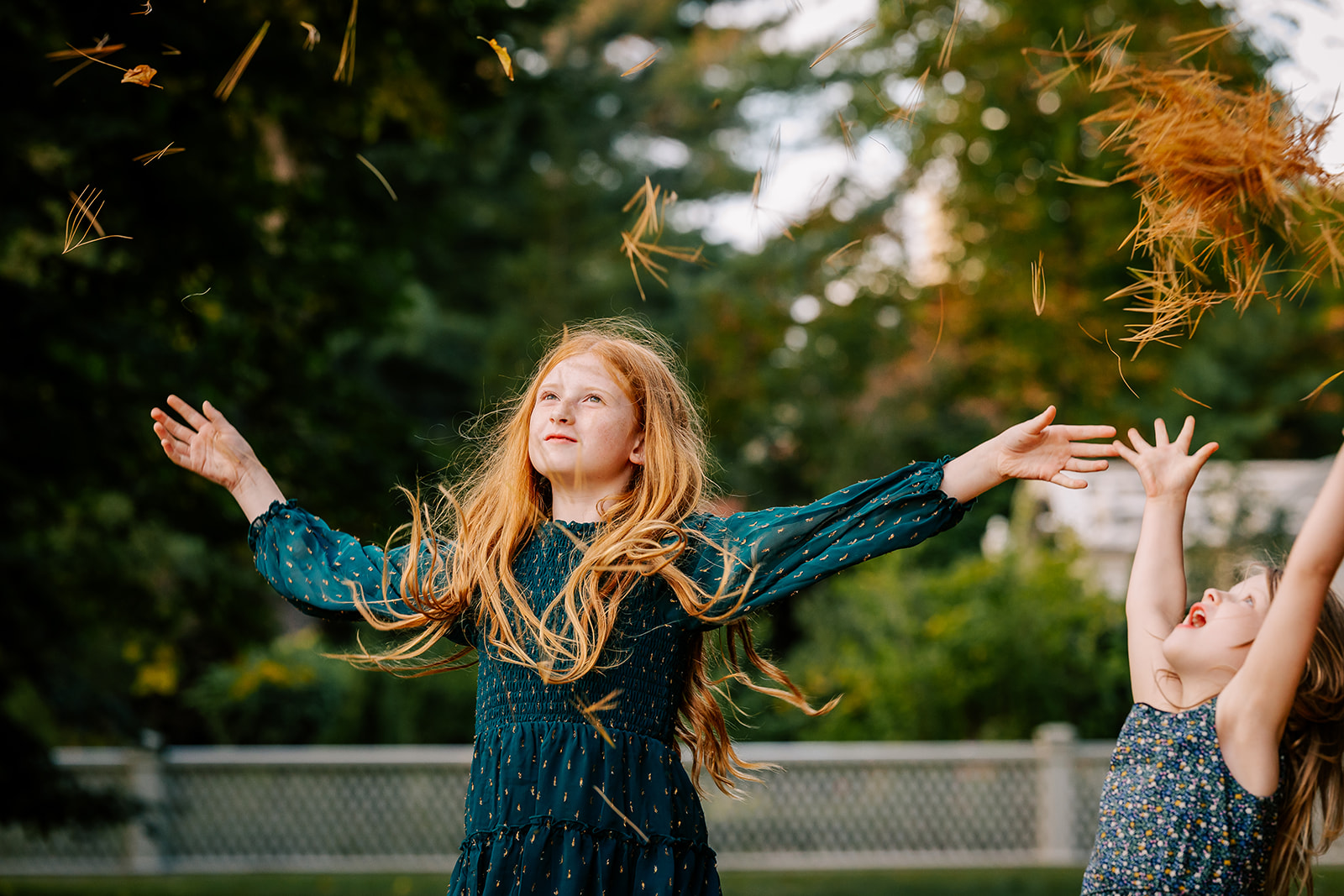 A young girl and her younger sister throw pine needles in the air while playing in a park and staying at kid-friendly hotels in Boston