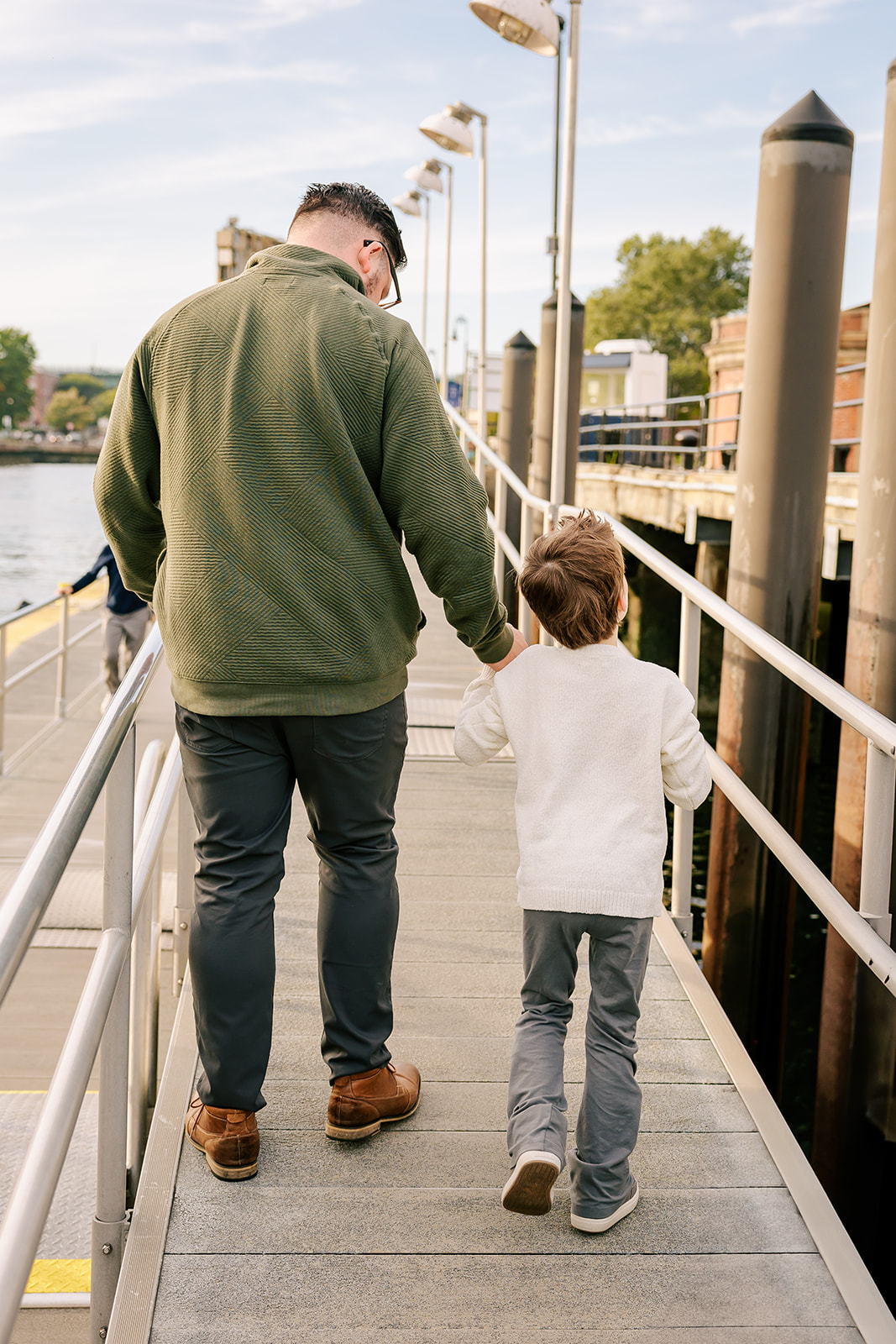 A dad walks with his child holding hands up a dock on the water