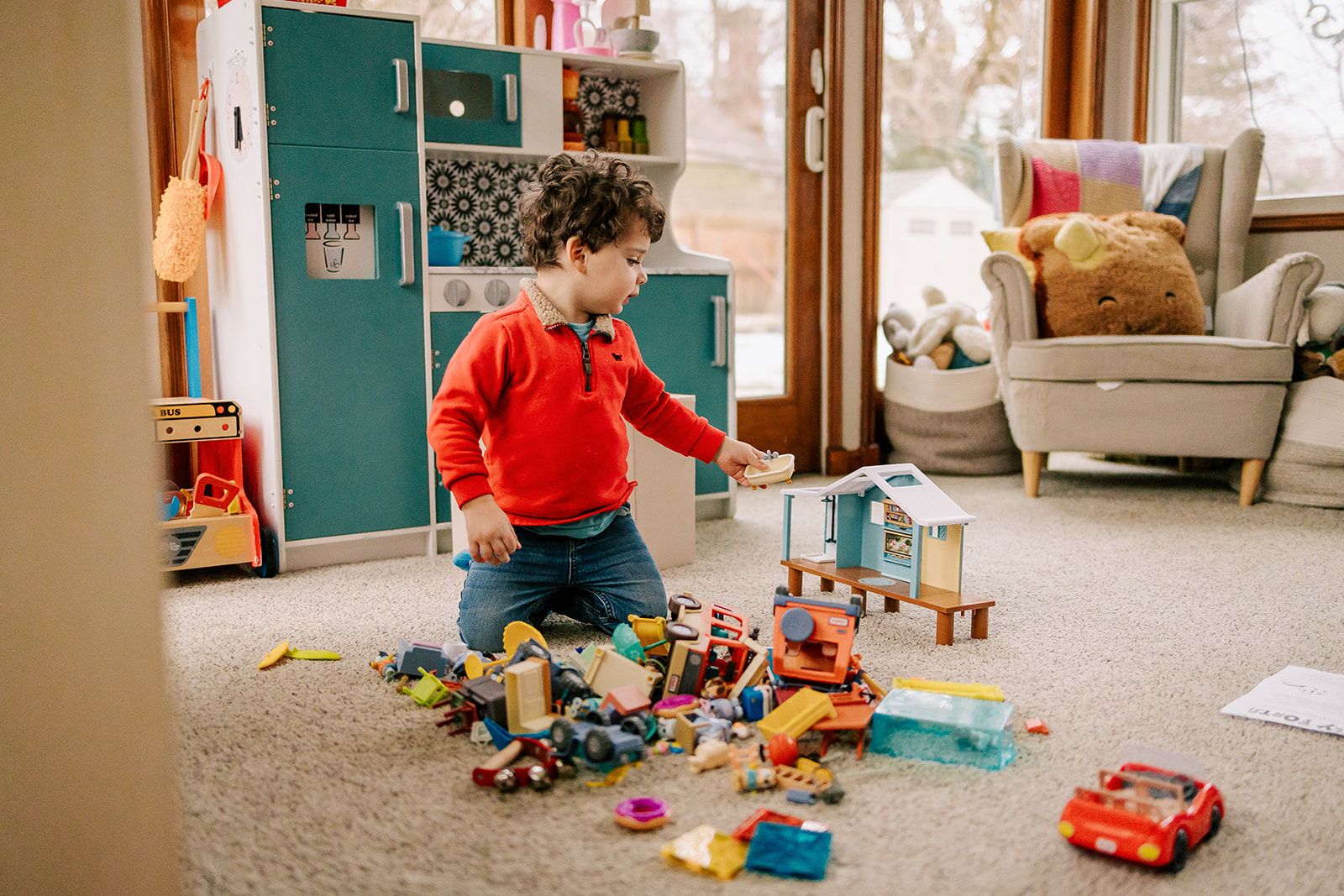 A happy boy plays house with a toy set in a living room of windows