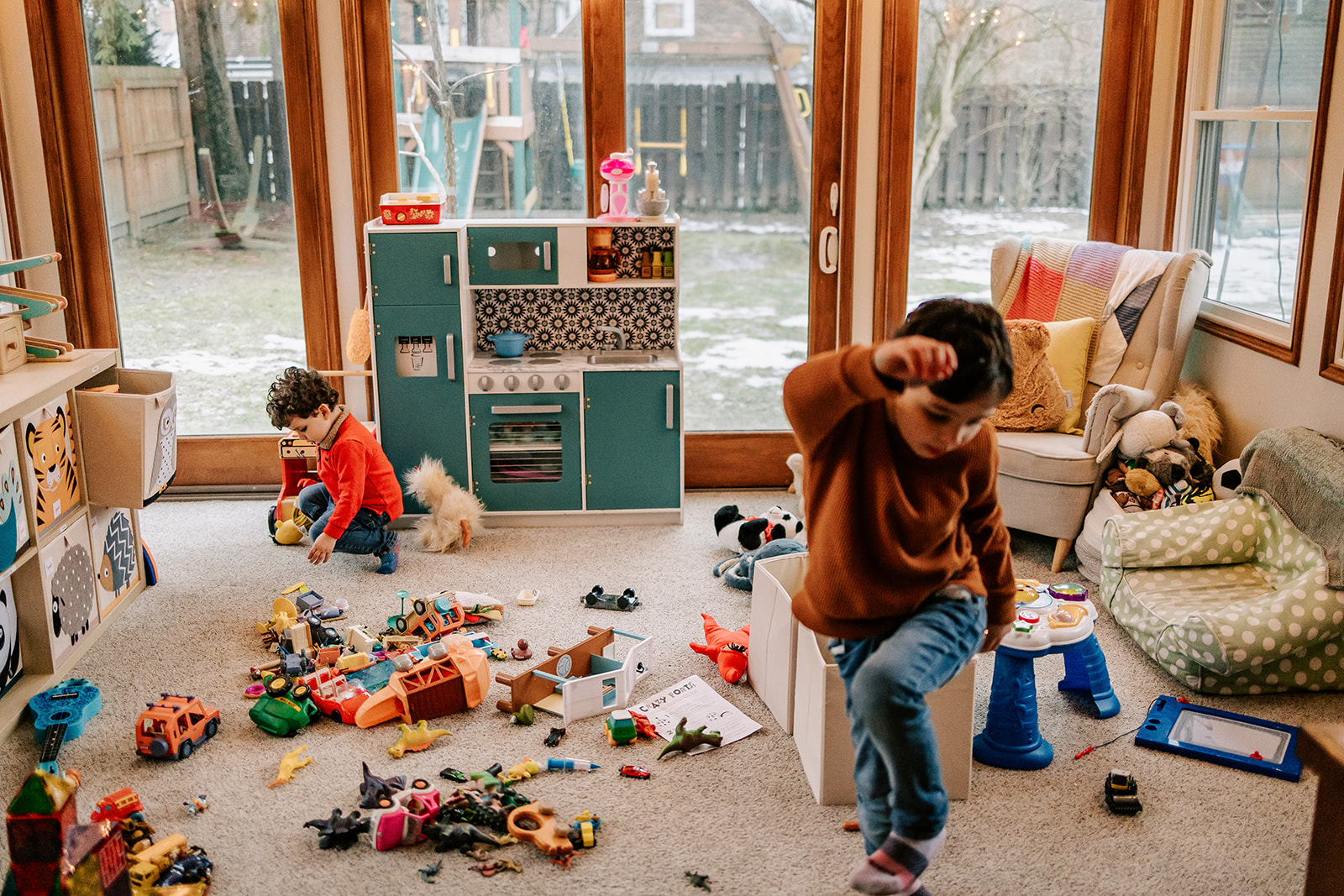 Two toddler boys play in a sun room full of toys in jeans and red sweaters after visiting Montessori Schools in Boston