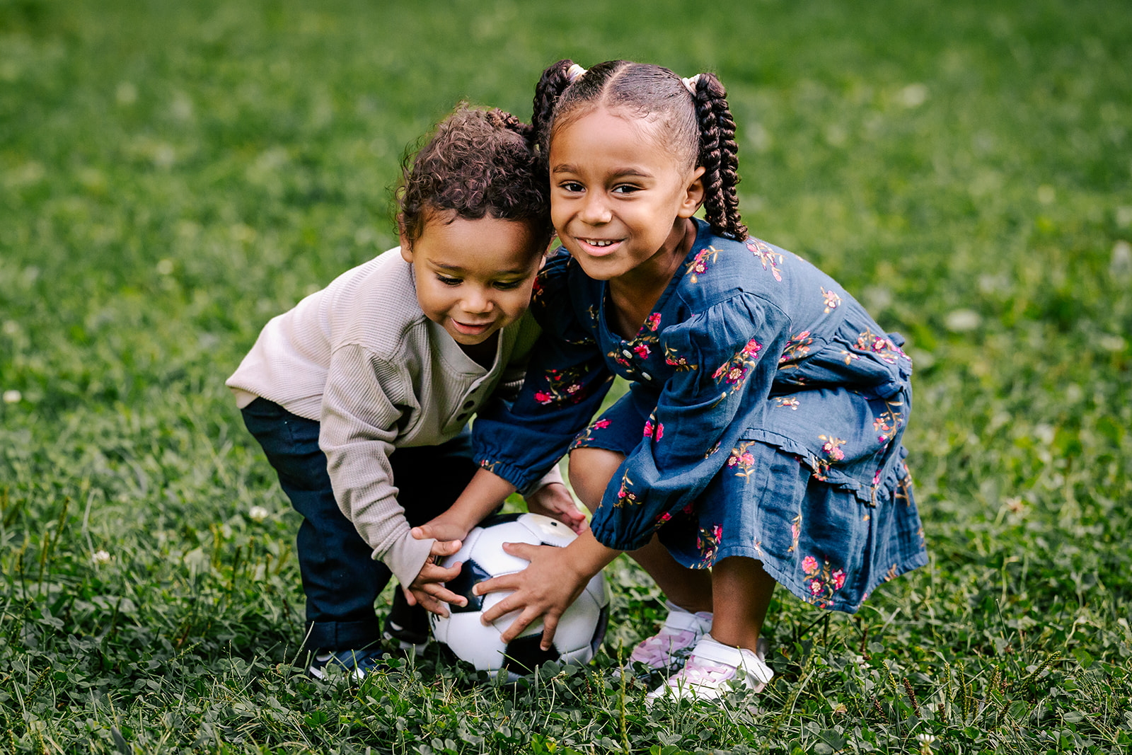 A young girl plays with a soccer ball with her baby brother in a park lawn