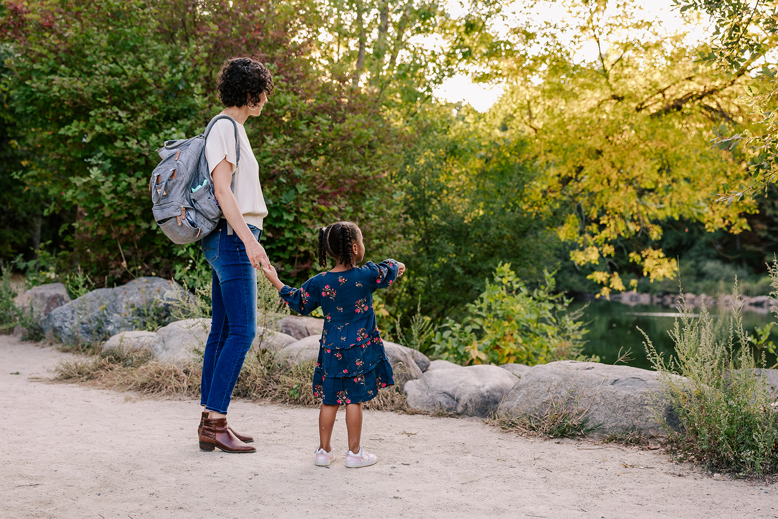 A mom and her toddler daughter explore a park pond at sunset after exploring private preschools in Boston