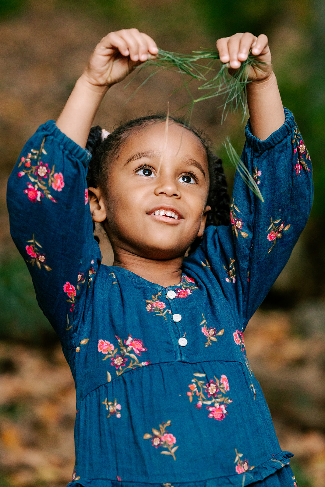 A young girl in a blue dress plays with grass in a park after visiting private preschools in Boston