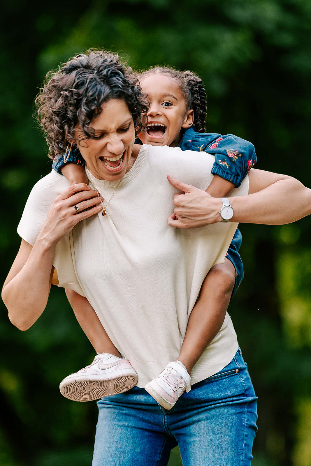 A happy toddler laughs while climbing on mom's back after visiting private preschools in Boston