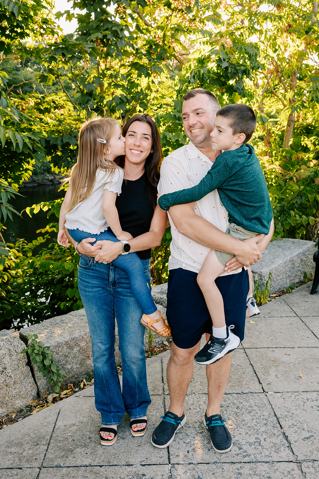 Happy mom and dad carry their toddler son and daughter in a park at sunset