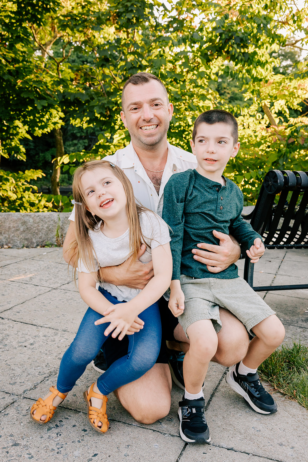 A happy dad hugs his sone and daughter in a park before visiting a splash pad in Boston