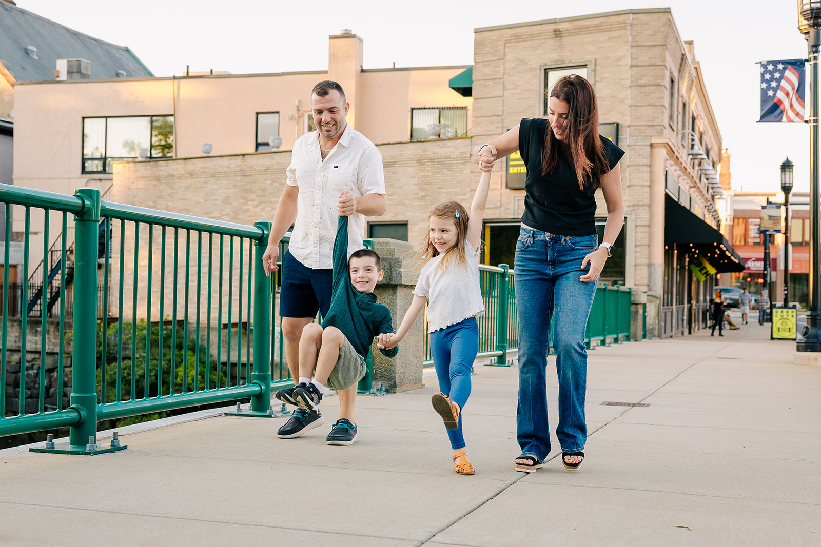 Happy toddler brother and sister play while walking the street holding mom and dad's hands before visiting splash pad in Boston