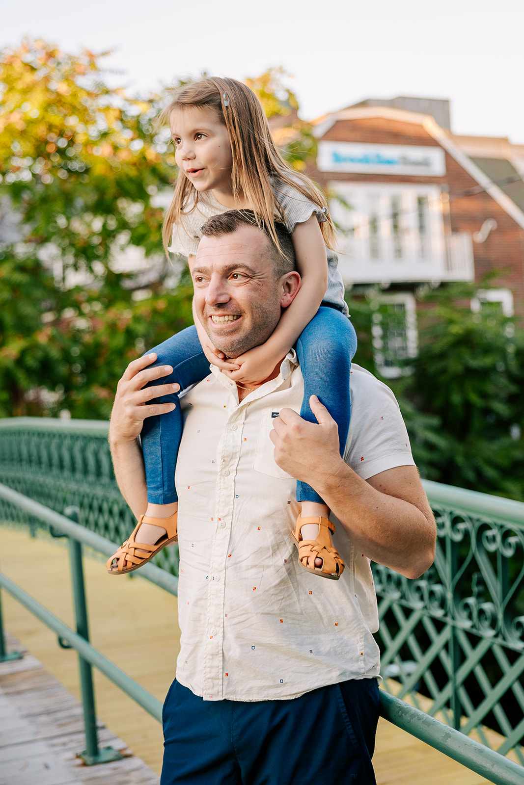 A happy toddler girl rides dad's shoulders in a park on their way to a splash pad in Boston