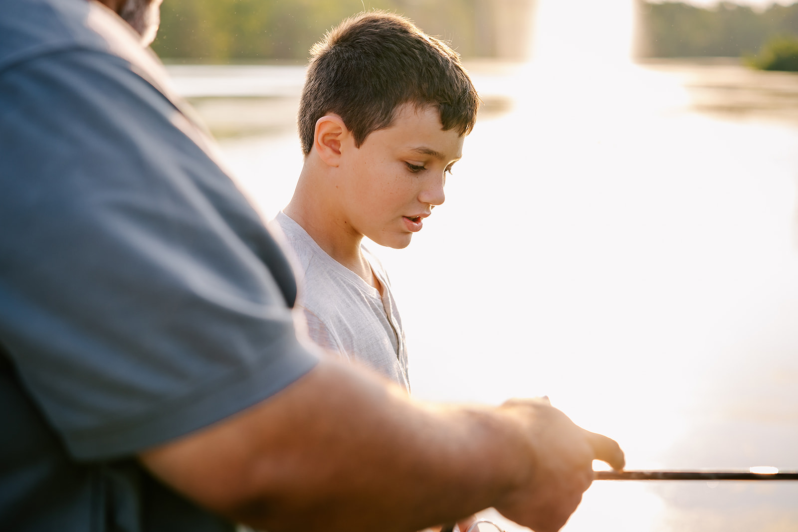 A dad helps his young son fish a pond after some summer camps in Boston