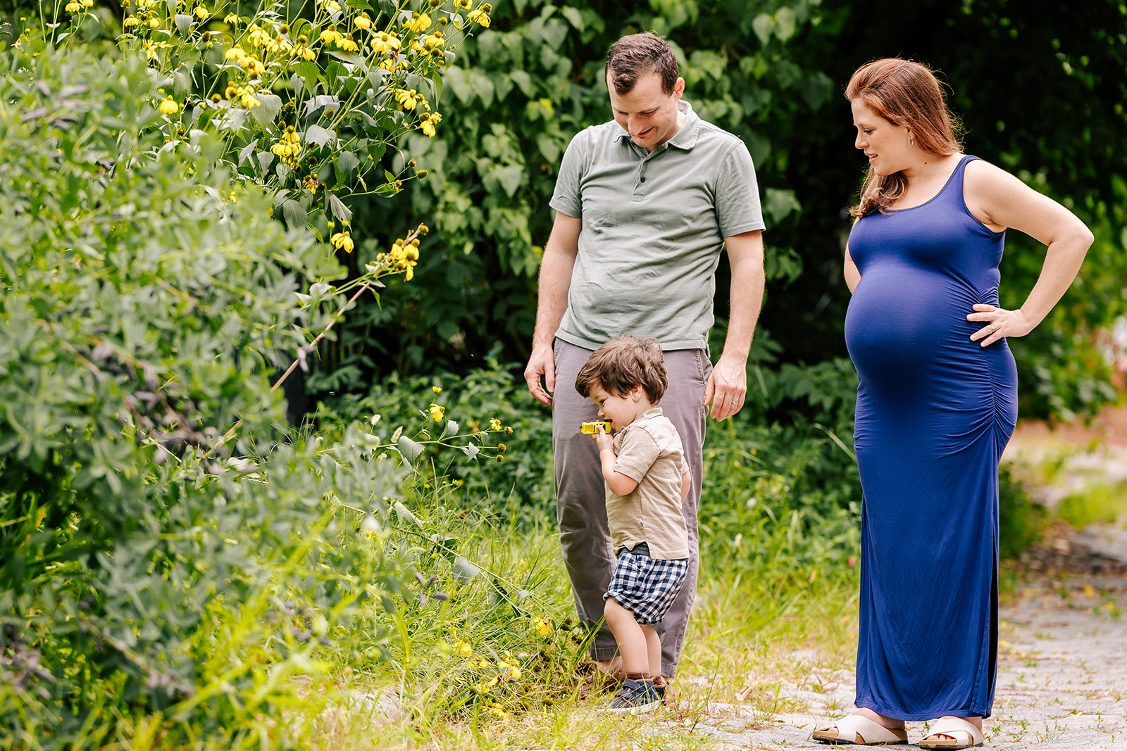 A pregnant mom and dad explore a park trail with their toddler son