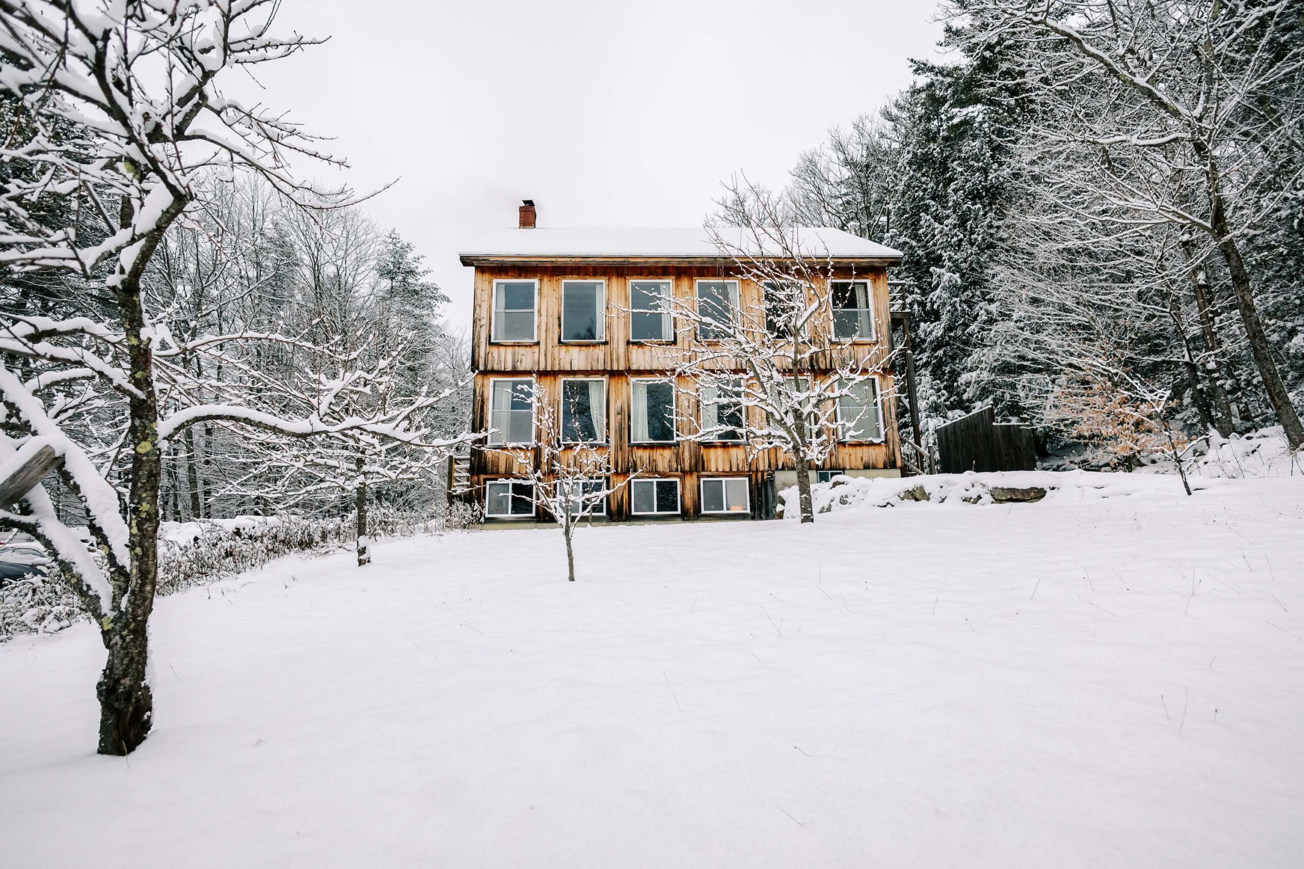 Two story wooden cabin set in the woods, surrounded by snow.