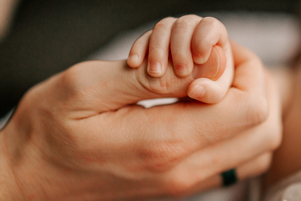 Close-up of a father's hand with his newborn daughter's tiny fist wrapped around his thumb