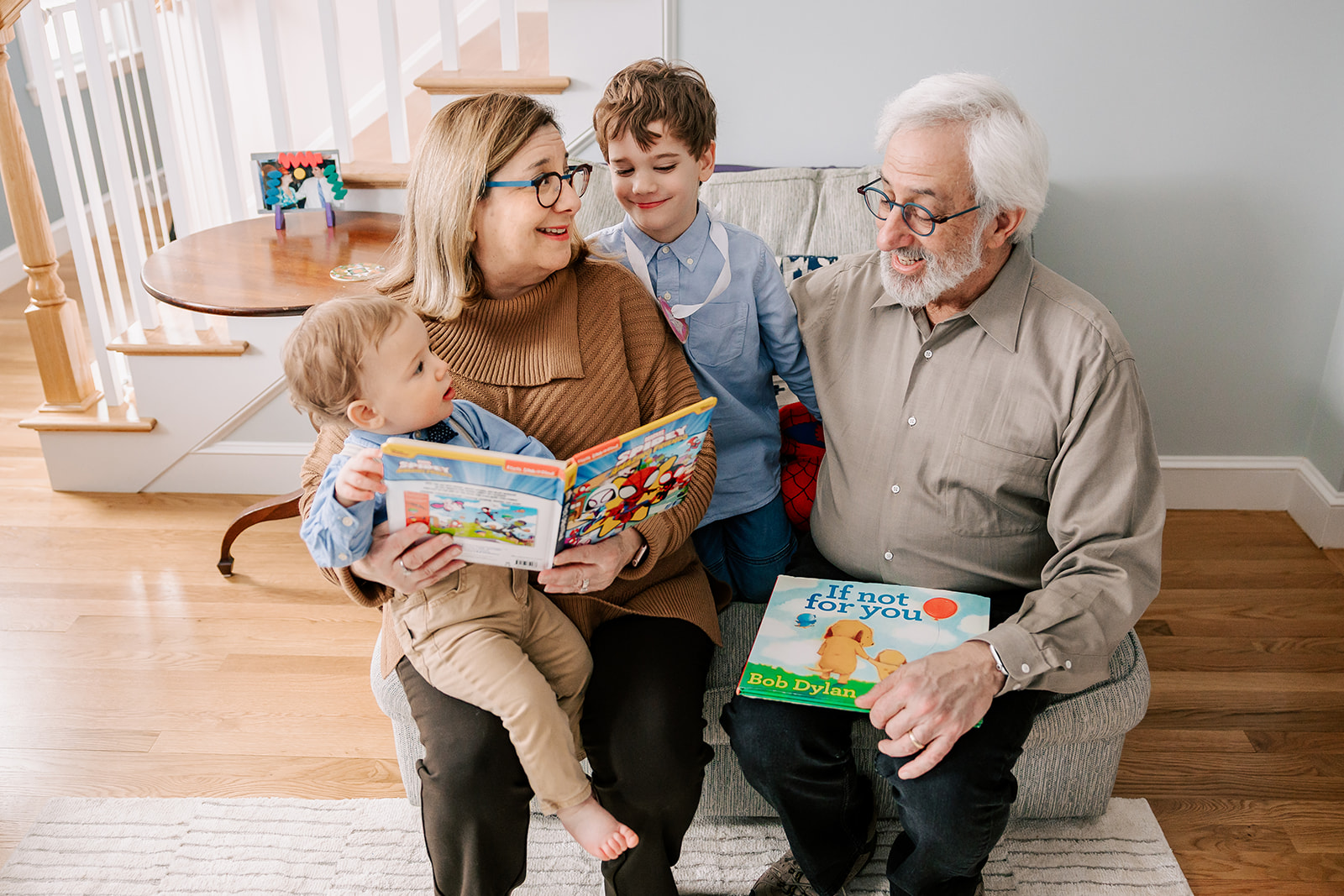 Toddler brothers sit with grandparents on a chair reading books with big smiles