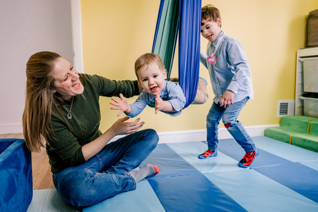 A toddler boy swings in a silk with mom and bigger brother helping